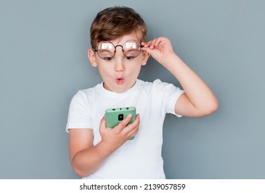 Shocked child boy using smartphone and taking off glasses on gray background - Powered by Shutterstock