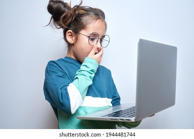 Shocked child girl with open mouth and bulging eyes looks at a computer laptop screen. Internet porn censorship concept, adult content 18+