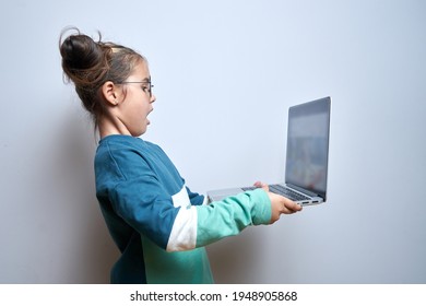Shocked child girl with open mouth and bulging eyes looks at a computer laptop screen. Internet porn censorship concept, adult content 18+