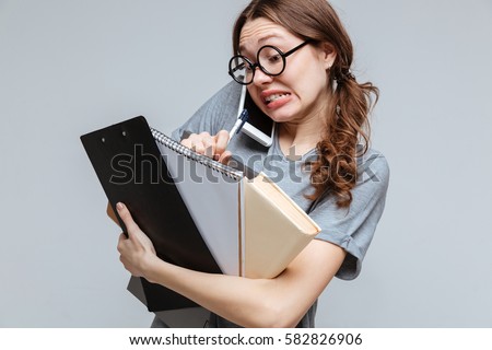 Shocked Clumsy female nerd which talking on phone and holding laptop, clipboard and notebook