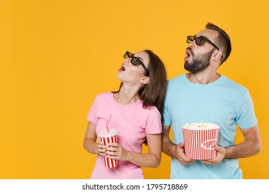 Shocked couple friends man woman in blue pink t-shirts 3d glasses isolated on yellow background. People in cinema, lifestyle concept. Watching movie film, hold bucket popcorn, cup soda, looking up - Powered by Shutterstock