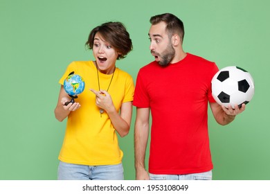 Shocked Couple Friends Sport Family Woman Man Football Fans In T-shirts Cheer Up Support Favorite Team With Soccer Ball Pointing Index Finger On Earth World Globe Isolated On Green Background Studio