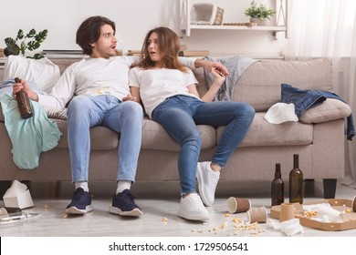 Shocked Couple Waking Up In Messy Room After Celebration Party At Home, Floor Covered With Garbage And Empty Bottles