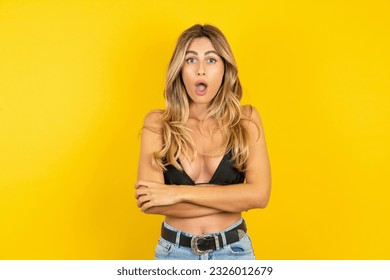 Shocked embarrassed Young blonde woman on vacation wearing bikini over yellow background keeps mouth widely opened. Hears unbelievable novelty stares in stupor - Powered by Shutterstock