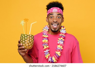 Shocked Excited Fun Young Man 20s He Wearing Pink T-shirt Hawaiian Lei Near Hotel Pool Drink Straw Pineapple Cocktail Juice Isolated On Plain Yellow Background Studio. Summer Vacation Sea Rest Concept