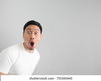 Shocked face of Asian man in white shirt on grey background.
