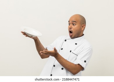 Shocked Face. Young Handsome Asian Man Chef In Uniform Spilling Empty Plate Delicious Dish Menu Accidental Drop On Isolated. Cooking Indian Man Occupation Chef People In Kitchen Restaurant And Hotel.