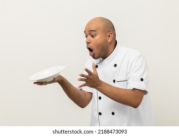 Shocked Face. Young Handsome Asian Man Chef In Uniform Spilling Empty Plate Delicious Dish Menu Accidental Drop On Isolated. Cooking Indian Man Occupation Chef People In Kitchen Restaurant And Hotel.