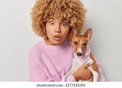 Shocked female pet owner stares at camera with omg expression poses with breed dog cannot believe own eyes dressed in knitted jumper isolated over white background. Domestic animals and friendship