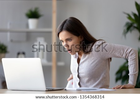 Shocked female sitting at desk looking at laptop screen rounding eyes surprised bad online news, stressed horrified frightened woman in panic with scared face, big trouble, unexpected results concept