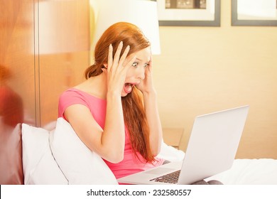 Shocked Funny Casual Young Woman Using Laptop Looking At Computer Screen Blown Away Lying In Bed At Home, Hotel. Human Face Expression, Emotion, Feeling, Perception, Body Language, Reaction