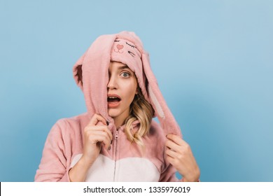 Shocked Girl Posing In Pink Bunny Suit. Studio Shot Of Amazed Female Model In Cute Kigurumi Isolated On Blue Background.