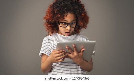 Shocked kid girl with tablet pc, gray studio background