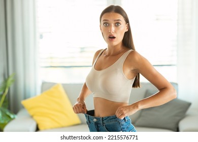 Shocked Lady After Great Weight Loss Posing Wearing Old Too Big Jeans For Comparison Looking At Camera Standing At Home. Slimming Result, Successful Dieting Concept