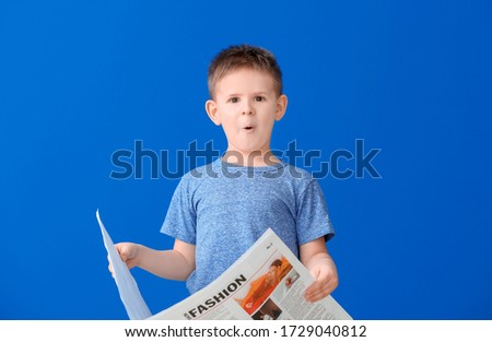 Shocked little boy reading newspaper on color background
