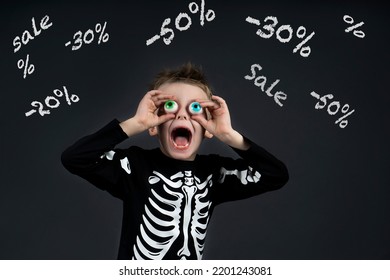 Shocked Little Halloween Boy With Toy Eyes Looking Up And At Sale Sale -50% -30  Open Mouth With Crazy And Delighted In Halloween Costume Skeleton On Dark Background Sale Concept. Black Friday Kids