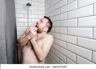 Shocked man looks at a watering can in the shower room, from which, unexpectedly, cold water is pouring.