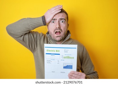 Shocked Man Reading Some Bills Energy Expenses Isolated On Yellow Background