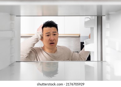 Shocked Middle Aged Chinese Man Looking Inside Empty Fridge And Touching His Head, Lack Of Food, Need For Shopping, Suffering From Financial Hangover While Pandemic, Shot From Inside, Copy Space