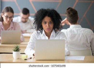 Shocked Mixed Race Woman Looking At Laptop In Shared Office, Stressed Black Female Employee Terrified Reading Online News, Afro American Student Afraid Of Cyber Bullying Bad Email Or Computer Problem