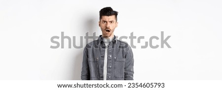 Shocked and offended man frowning, looking at camera with opened mouth, feeling hurt by cruel words, standing disappointed on white background.