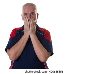 Shocked Older Man Wearing Bowling Shirt Holds Both Hands To His Face Against A White Background