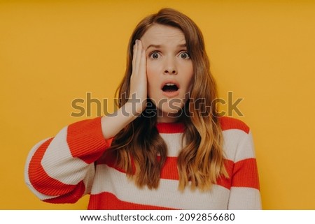 Shocked overwhelmed young millennial women in striped sweater touching head with one hand and looking at camera with wide open mouth and big eyes, hearing something unbelievable from friend Stock photo © 