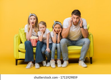 Shocked Parents And Kids Watching Movie On Sofa With Popcorn Bucket On Yellow