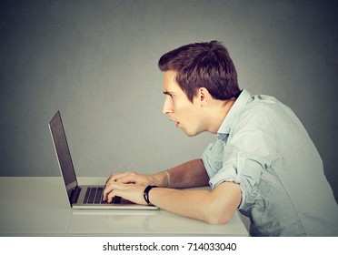 Shocked Perplexed Man Sitting In Front Of Laptop Computer Looking At Screen Isolated On Gray Wall Background. Face Expression Emotion Feelings