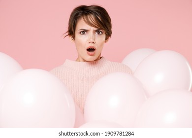 Shocked perplexed sad young brunette woman 20s in knitted casual sweater posing celebrating hold air balloons isolated on pastel pink background studio. Birthday holiday party, people emotions concept
