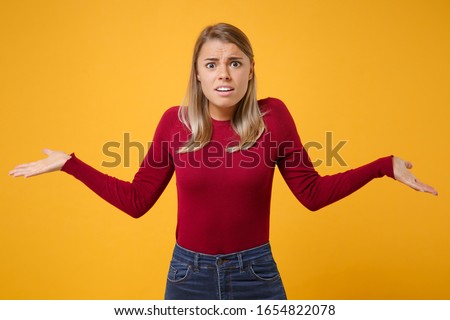 Shocked perplexed young blonde woman girl in casual clothes posing isolated on yellow orange wall background studio portrait. People emotions lifestyle concept. Mock up copy space. Spreading hands