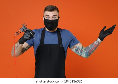 Shocked Professional Tattooer Master Artist Tattooed Man In T-shirt Apron Face Mask Hold Machine Black Ink In Jar Equipment For Making Tattoo Art On Body Spreading Hands Isolated On Brown Background
