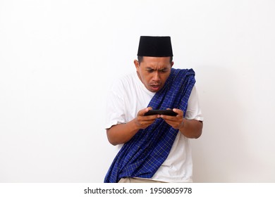 Shocked And Sad Asian Man Standing While Holding A Cellular Phone. He Playing And Lose A Game. Isolated On White Background.