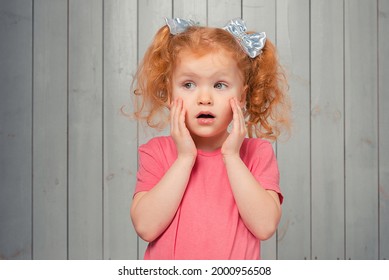 Shocked and scared redhead little girl 4-6 years old, staring startled at left and frightened, afraid of something scary. Studio shot, light wooden background