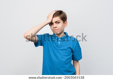 Shocked Serious boy 12-14 years old in casual blue t shirt, look puzzled and amazed, holding hand on head, staring at problem, forgot remember something, standing against light gray background, isolat