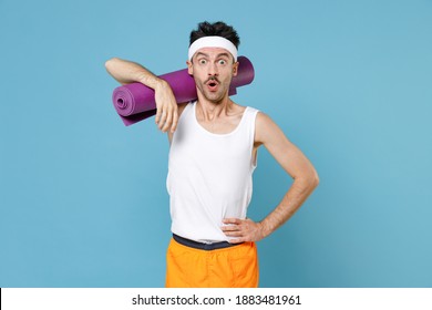 Shocked Strong Sporty Fitness Man With Thin Skinny Body Sportsman In White Headband Shirt Shorts Hold Yoga Mat Keeping Mouth Open Isolated On Blue Background. Workout Gym Sport Motivation Concept