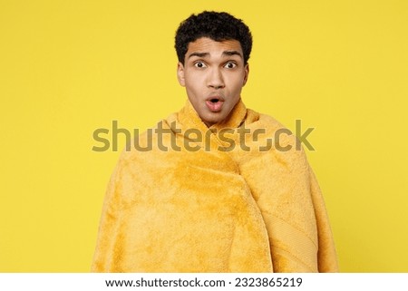 Shocked stupefied sad astonished young man wrapped in towel relaxing near hotel pool look camera with opened mouth isolated on plain yellow color background. Summer vacation sea rest sun tan concept