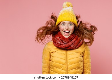 Shocked surprised amazed young woman 20s wears yellow jacket hat mittens keeping mouth wide open jumping have fun enjoy fluttering hair isolated on plain pastel light pink background studio portrait