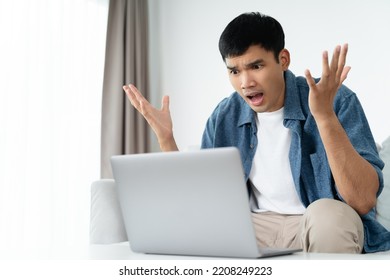 Shocked Surprised Asian Man Looking At Laptop Computer Screen Sitting In The Living Room.