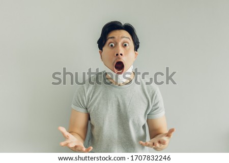 Shocked and surprised face of Asian man wearing hygienic mask in grey t-shirt.