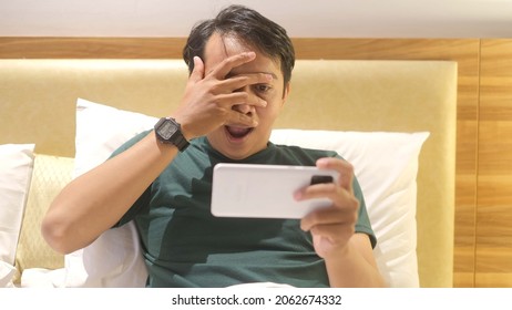 Shocked And Surprised Funny Face Of Asian Man Watch The Smartphone Alone At Night.