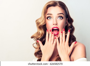 Shocked and surprised girl screaming covering  mouth her hands.Curly hair woman amazed.Beautiful girl  with curly hairstyle and red nails manicure.Presenting your product.Expressive facial expressions