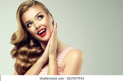 Shocked and surprised girl  smiling  looking to the side presenting  your product . Curly hair woman amazed .Beautiful girl  with red nails manicure. Expressive facial expressions. Pin up