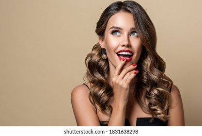 Shocked And Surprised Girl  Smiling  Looking To The Side Presenting  Your Product . Beautiful Curly Hair Woman Amazed ,   With Red Nails Manicure. Expressive Facial Expressions. Pin Up