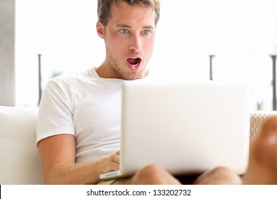 Shocked Surprised Man Looking At Laptop Computer Surprised And Amazed With Open Mouth And Big Eyes. Funny Young Male Model Sitting Outside On Sofa.