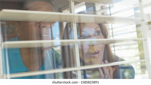 Shocked and surprised older couple looking out the window of their home. African American husband and wife shot through the window and blinds of their house looking out - Powered by Shutterstock