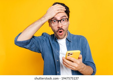 Shocked surprised puzzled caucasian handsome guy with glasses looking at the camera in amazement, holds smartphone in hand, won a victory, received unexpected news,stands on isolated orange background - Powered by Shutterstock