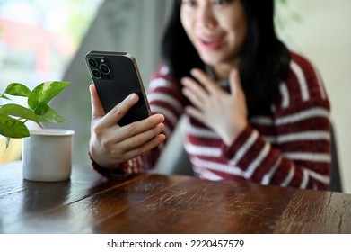 Shocked And Surprised Young Asian Woman Looking At Her Phone Screen, Receiving An Unexpected News While Relaxing In The Coffee Shop. Cropped Image