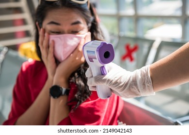 Shocked traveler with mask see high temperature result from Medical infrared thermometer on officer hand. woman in airport terminal disallow to departure due to covid-19 omicron virus. - Shutterstock ID 2149042143