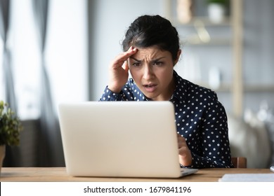 Shocked Unhappy Indian Woman Reading Bad News In Message, Stressed Young Female Looking At Laptop Screen, Touching Forehead, Frustrated Annoyed Girl Confused By Computer Problem Or Crash